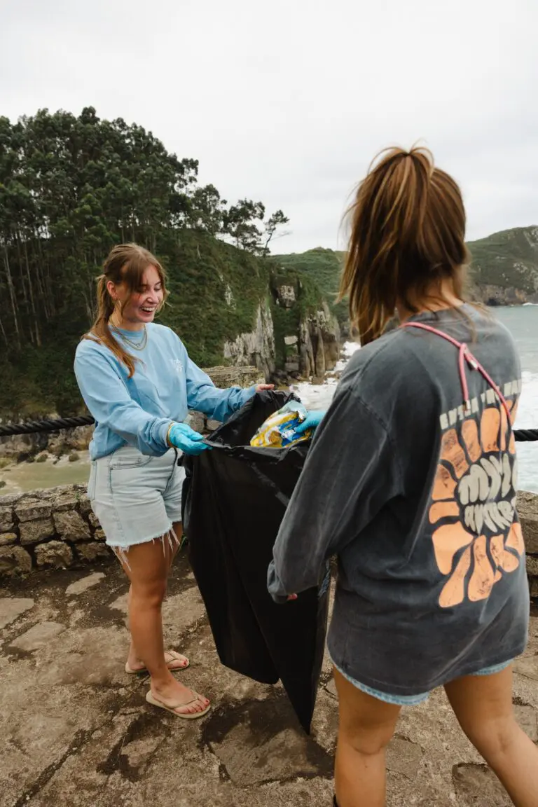 two young women collecting trash on a rocky coastline