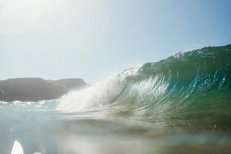 ocean wave breaking with sun flare and distant land